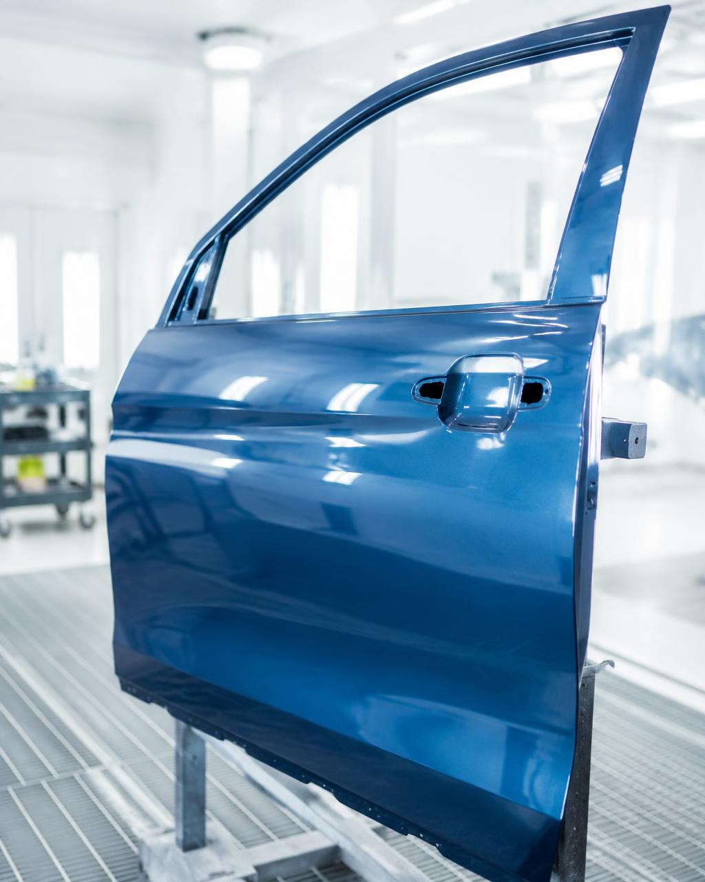 Freshly painted car door with a mirror-gloss finish inside a bright spray booth